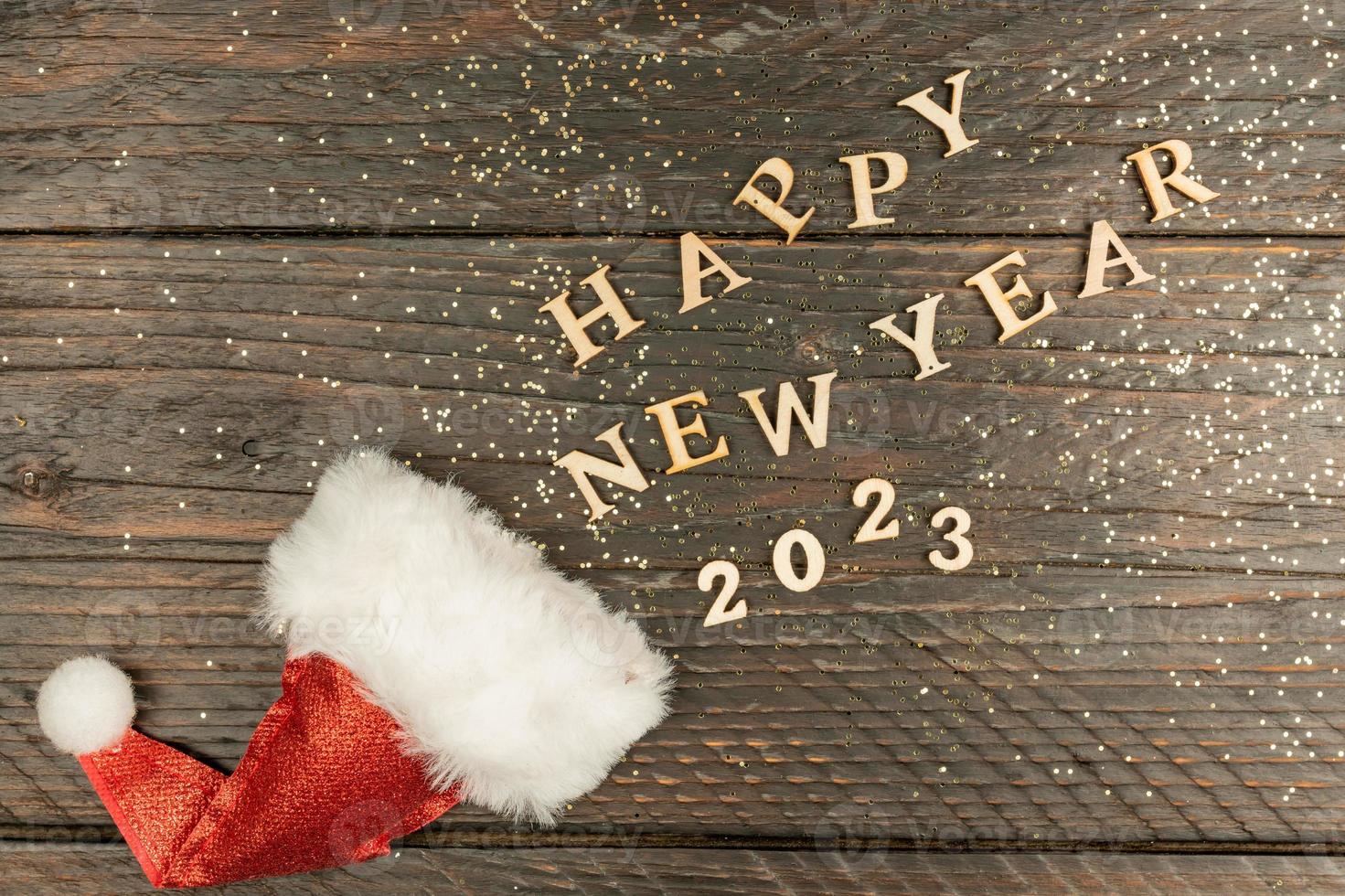 happy new year 2023 wooden letters scattered out of red Santa hat on wooden background. Festive greeting card. Holidays concept photo