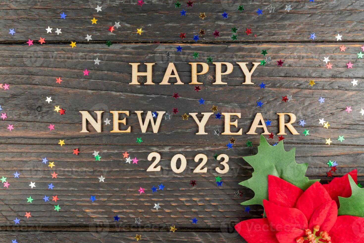 hapyy new year 2023 qoute made of wooen letters and red poinsettia flower as a symbol of chistmas and new year. Festive greeting card photo