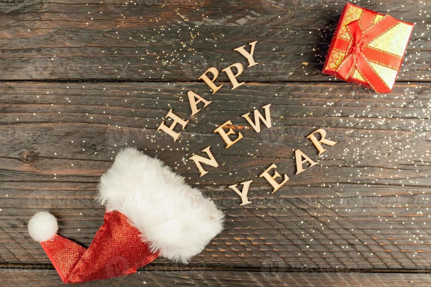 red Santa hat and happy new year scattered out of it. Red gift box next to the text. Festive greeting card, photo