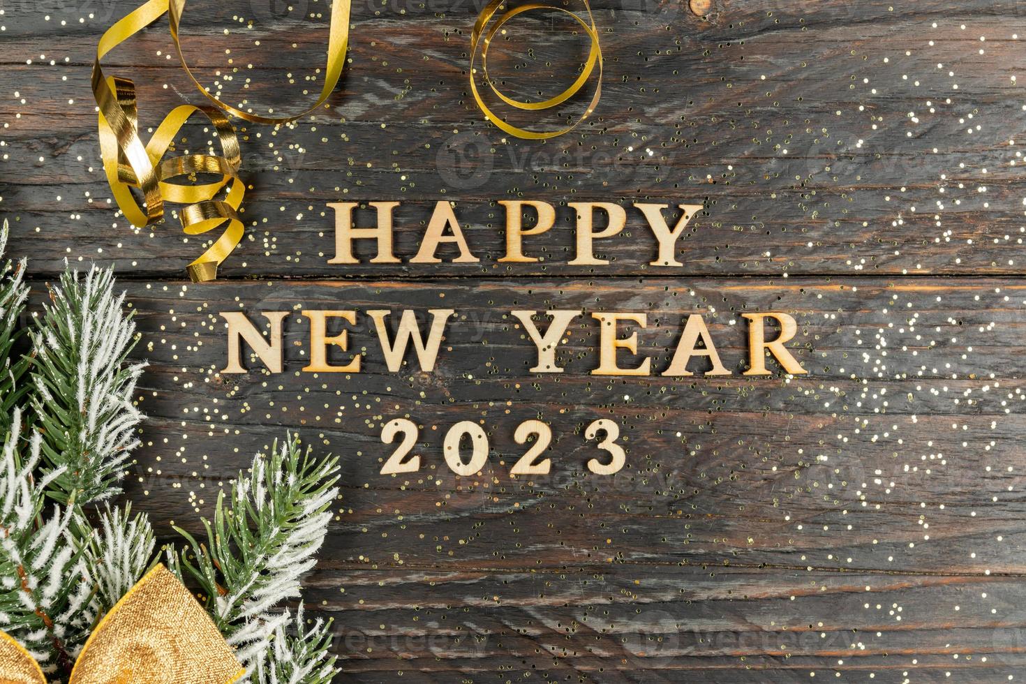 Happy New Year 2023. Quote made from wooden letters and numbers 2023 on wooden background dcorated fir tree branch with golden bow. Creative concept for new year greeting card photo