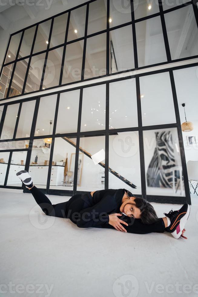 Young female wearing black sports suit exercising yoga pose indoors. photo