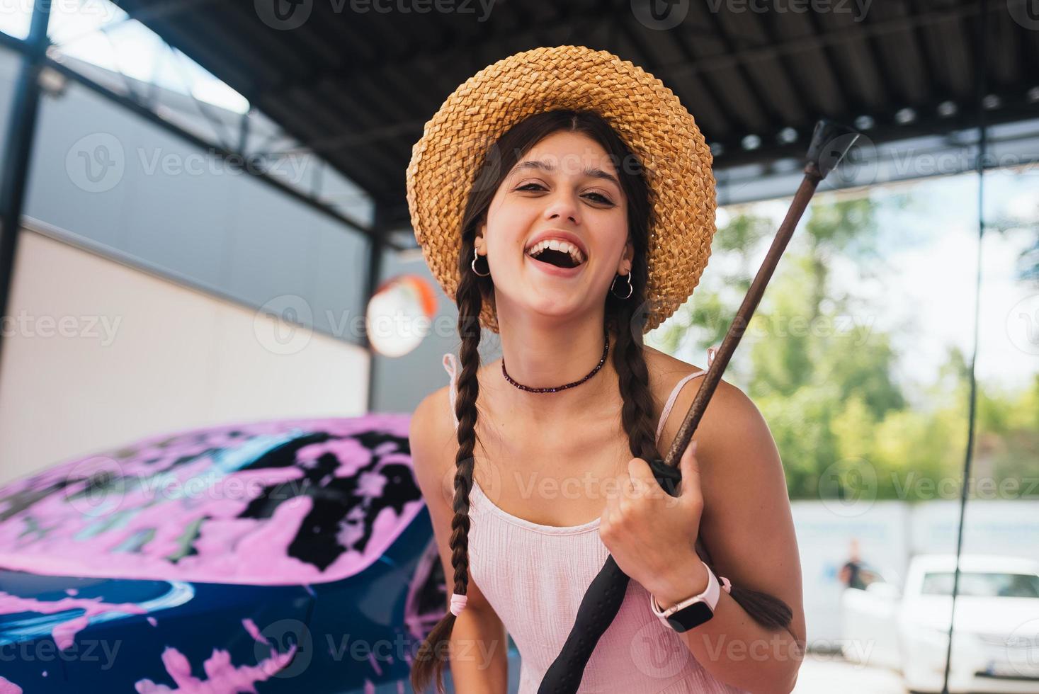 mujer con manguera parada junto a un auto cubierta de espuma rosa foto