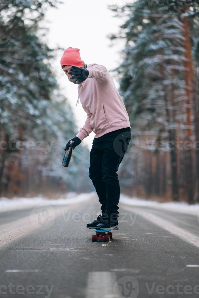 Skateboarder standing on the road in the middle of the forest, surrounded by snow photo