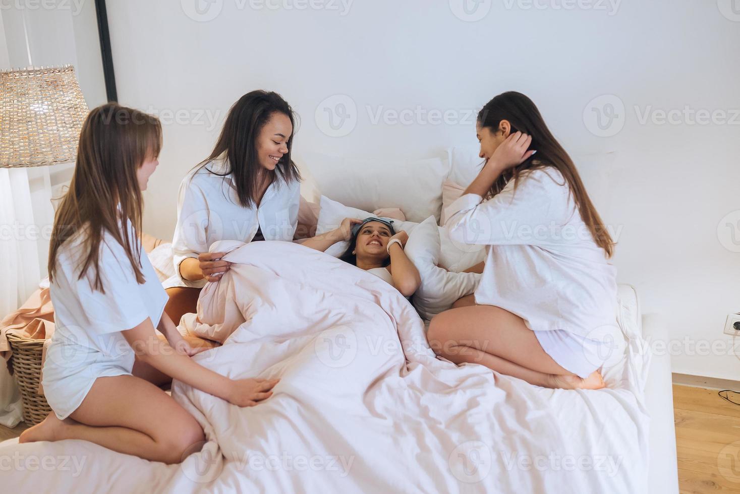 Positive young girls women friends indoors on bed at the hen party at home. photo