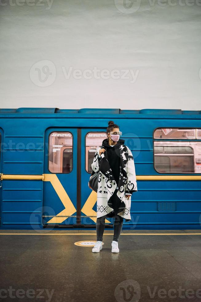 Young woman standing at station in medical protective mask photo
