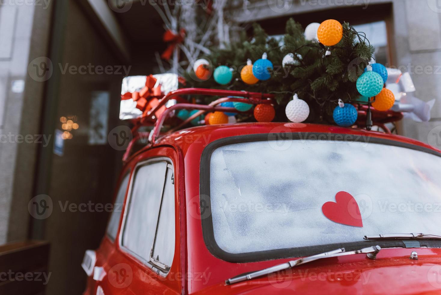 Red retro car with a Christmas tree fir tied to the roof. photo