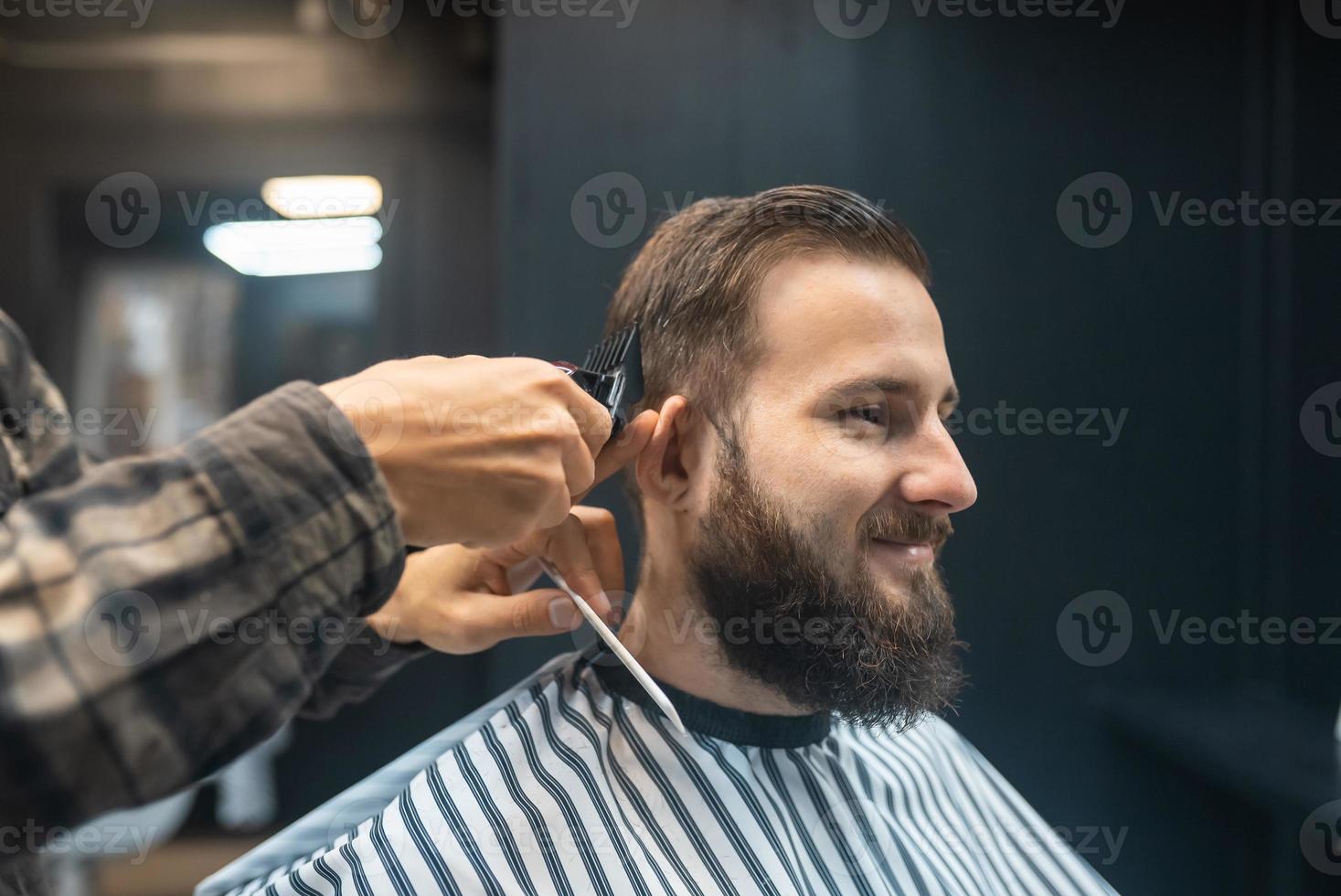 Master in barbershop makes men's haircutting with hair clipper photo