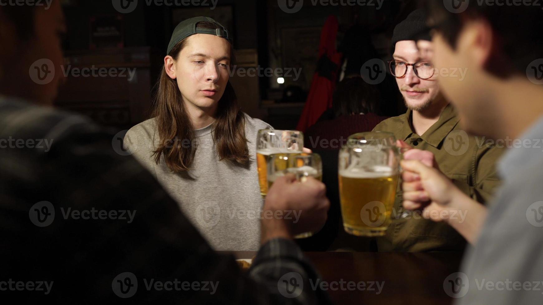 jóvenes amigos divirtiéndose juntos bebiendo cerveza y tintineando vasos en un pub. foto