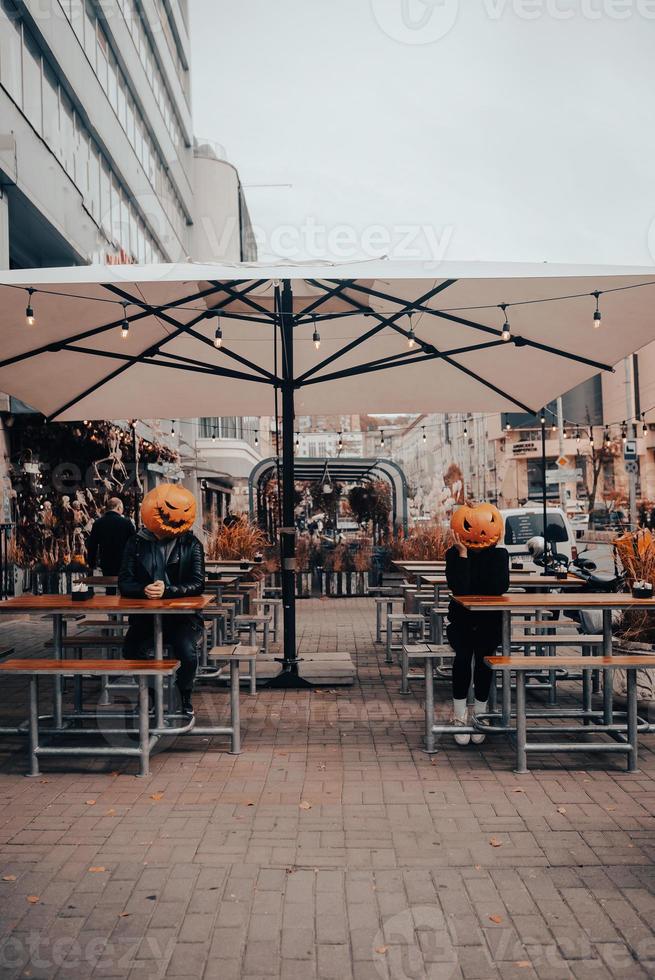 chico y chica con cabezas de calabaza en un café de la calle foto