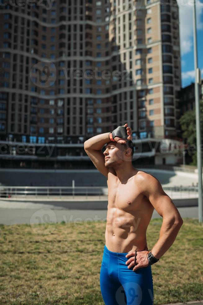 Muscular guy with a naked torso on the background of a tall building photo