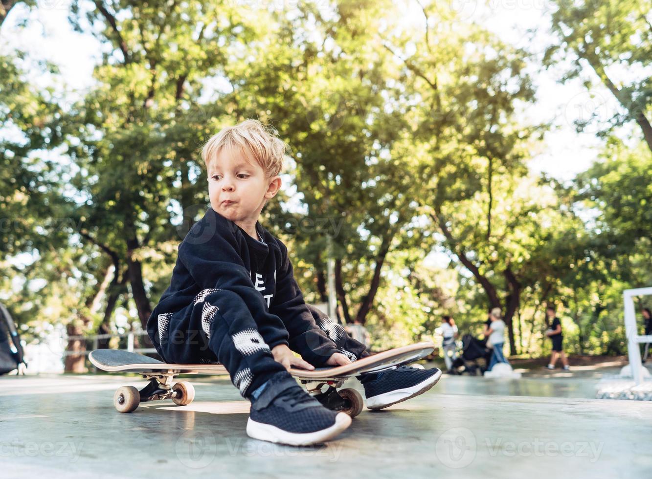 Young kid sitting in the park on a skateboard. photo