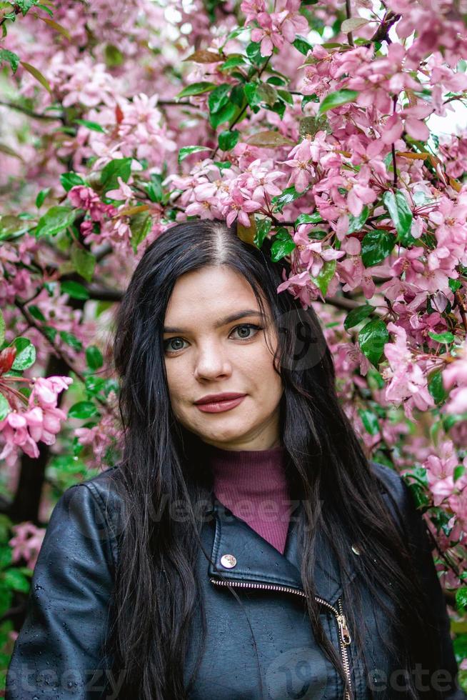 retrato de estilo de vida de una mujer joven y hermosa con flores de manzano rosa en clima lluvioso. foto