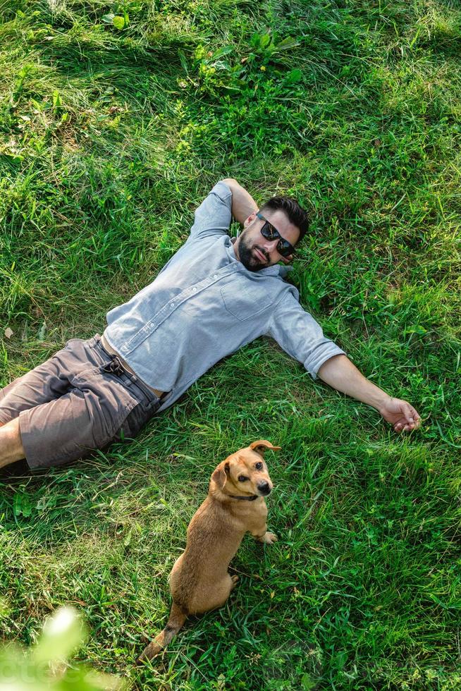 Top view of man and dog lying on green grass. Attractive European man resting with his dog. photo
