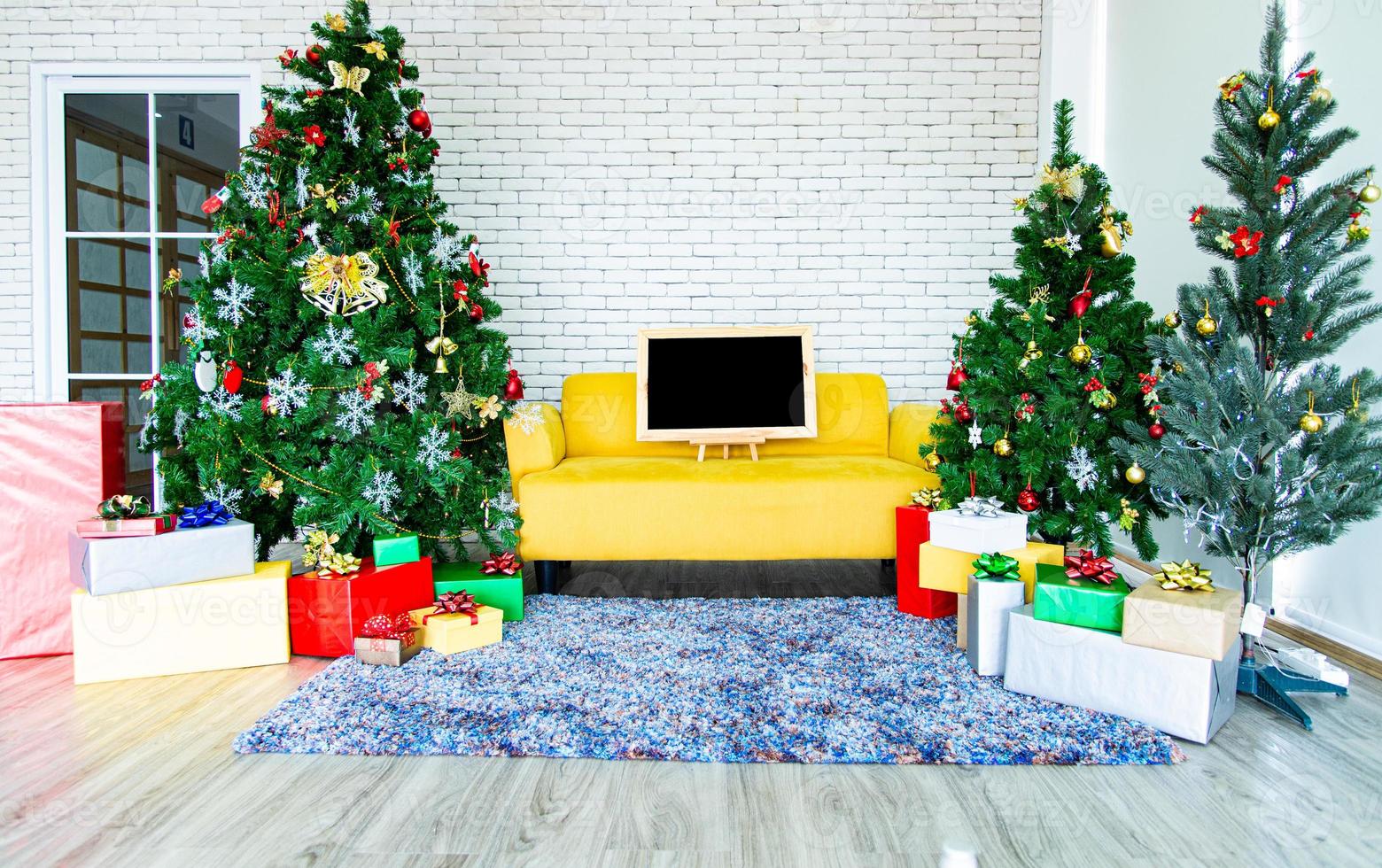 concepto de vacaciones de navidad y año nuevo. decoración de árboles de navidad con cintas de tablero negro bolas copos de nieve y adornos y cajas de regalo sobre pared de ladrillo blanco prepararse para la fiesta nocturna foto