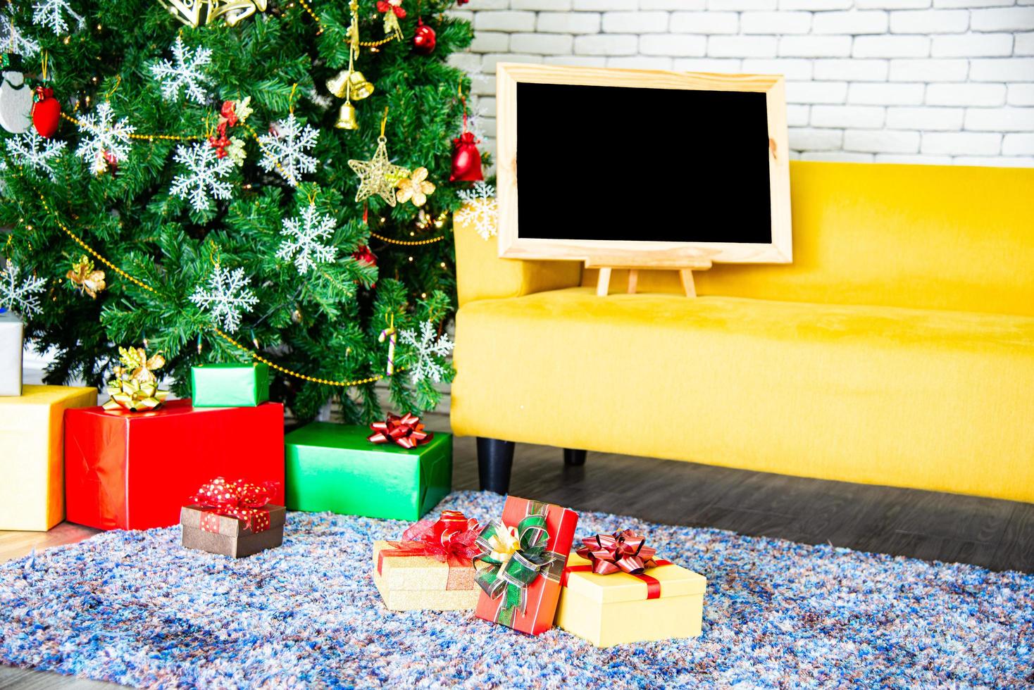 concepto de vacaciones de navidad y año nuevo. decoración de árboles de navidad con cintas de tablero negro bolas copos de nieve y adornos y cajas de regalo sobre pared de ladrillo blanco prepárate para la fiesta nocturna foto