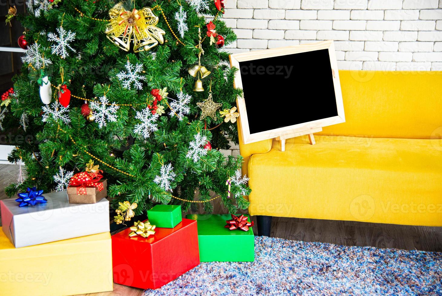 concepto de vacaciones de navidad y año nuevo. decoración de árboles de navidad con cintas de tablero negro bolas copos de nieve y adornos y cajas de regalo sobre pared de ladrillo blanco prepárate para la fiesta nocturna foto