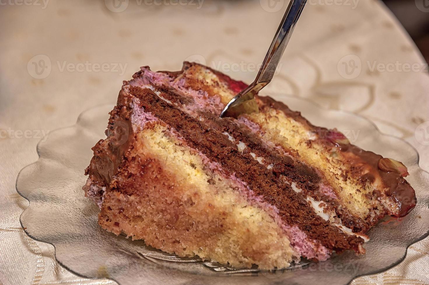 Close view of a delicate piece of chocolate cake, torte with nuts and fruits on a plate with a spoon. photo