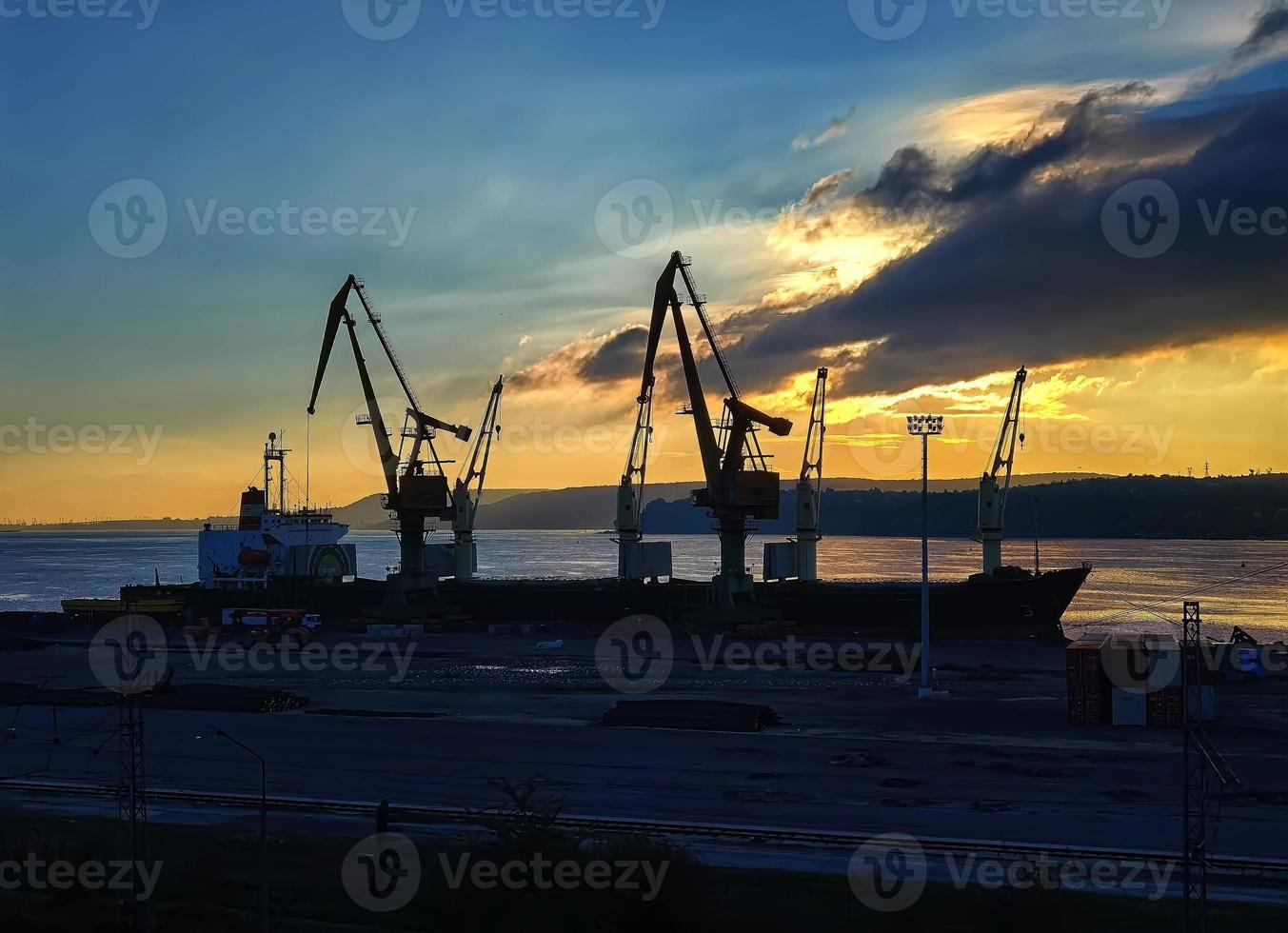 Silhouettes of cranes and ships at the port at sunset photo