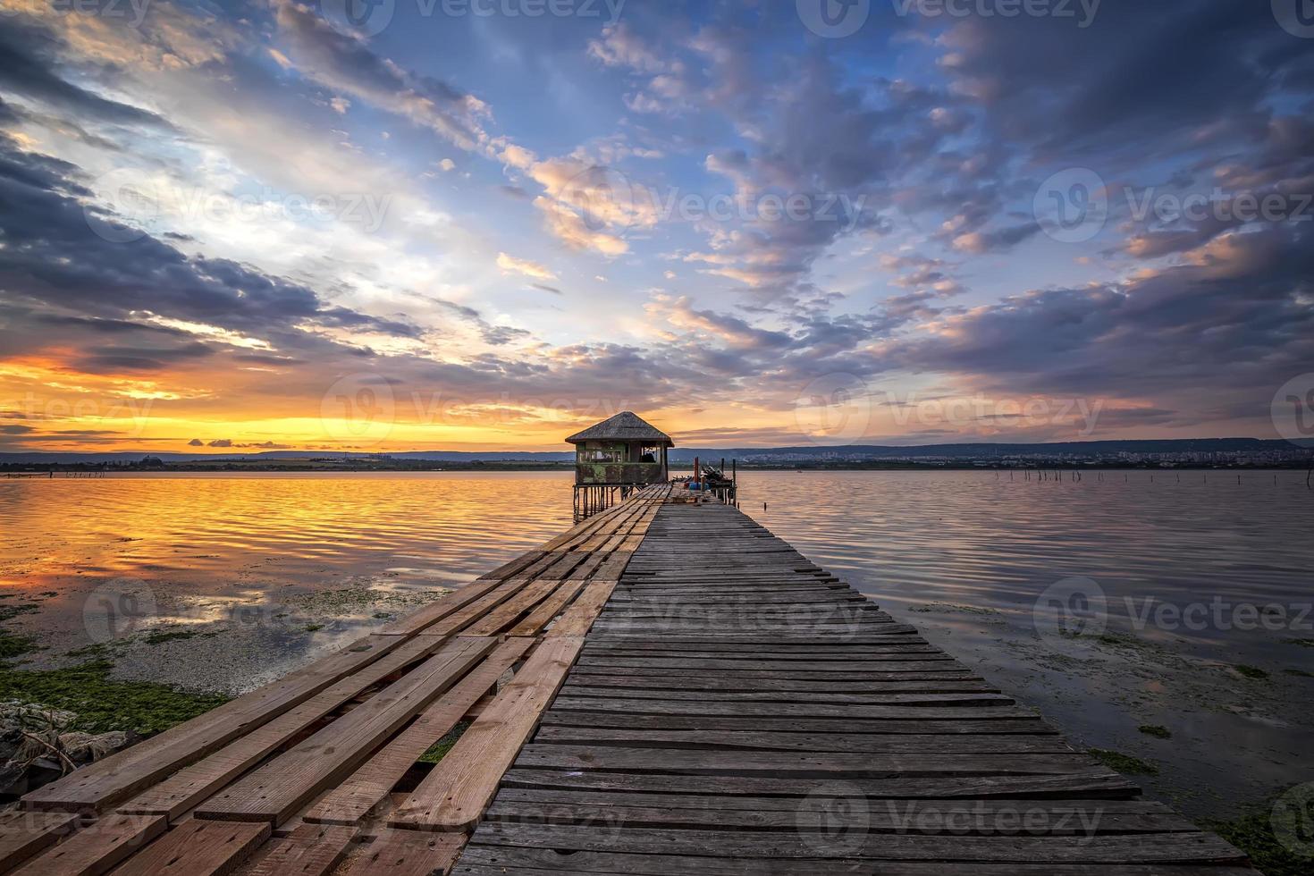 emocionante paisaje colorido de larga exposición en un lago con un muelle de madera y una pequeña casa al final. foto