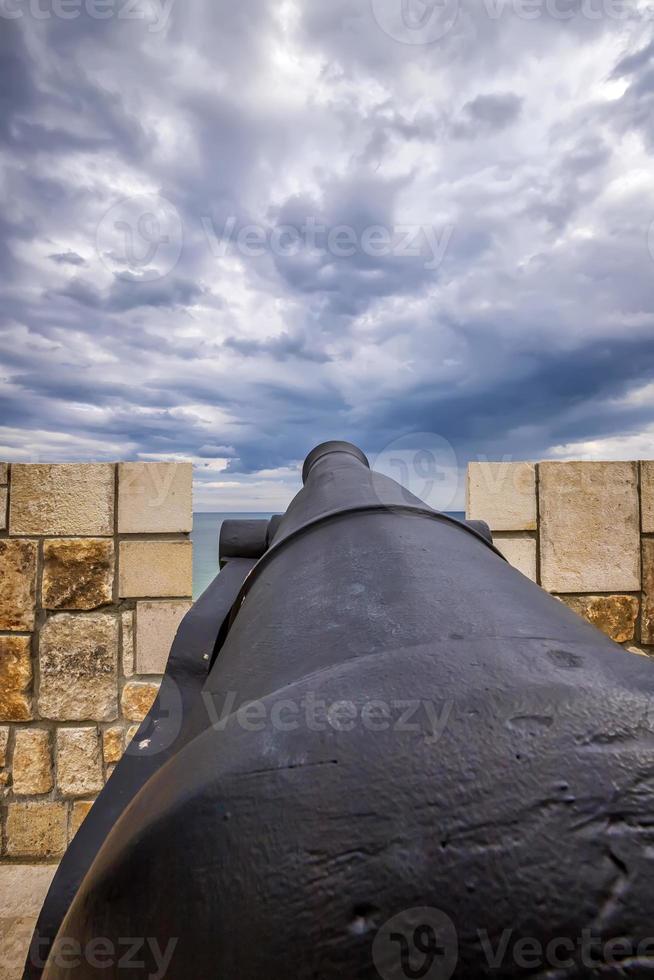 Old iron cannon pointing through an opening in a castle rampart. photo