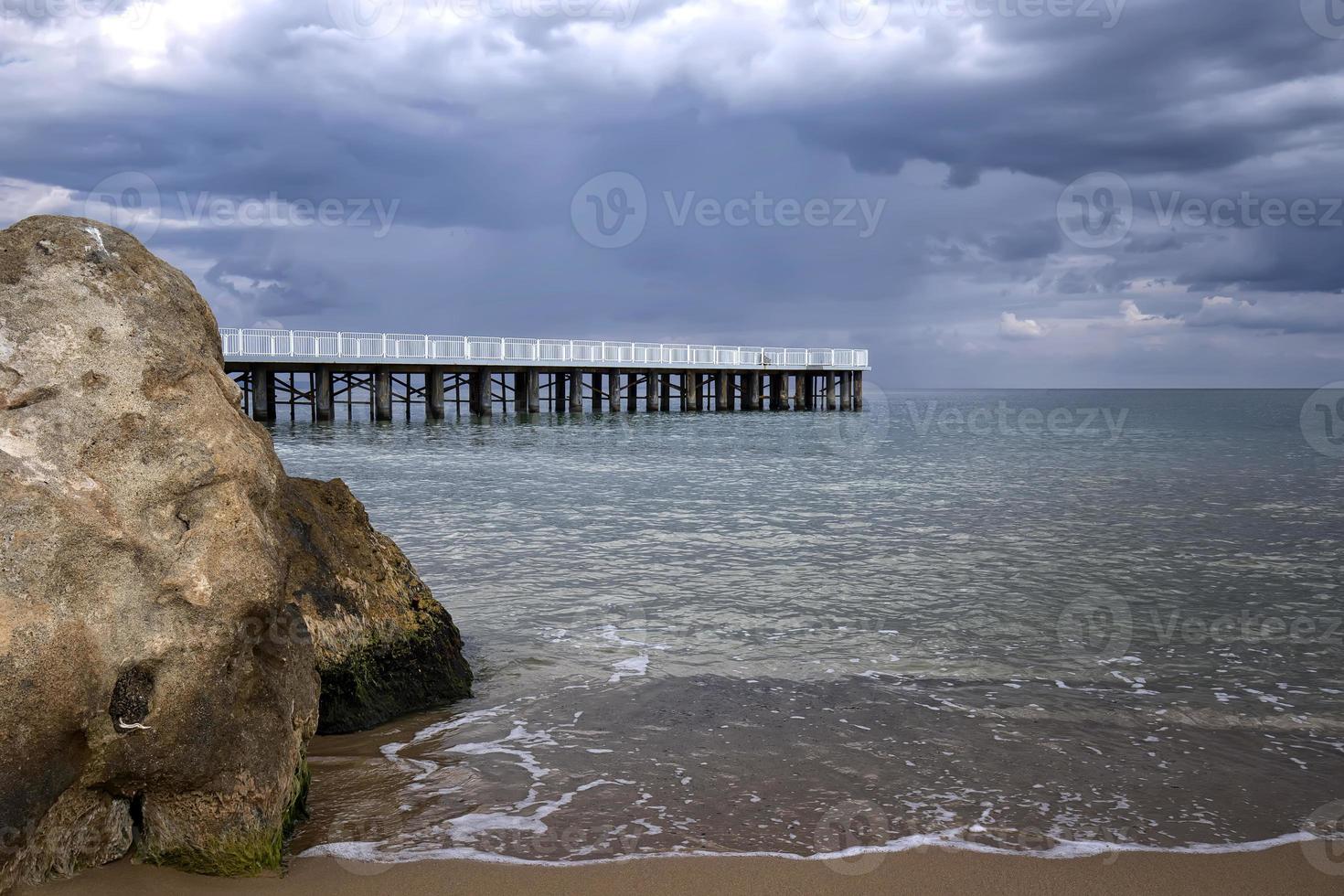 vista de ángulo bajo del mar con un muelle y una gran roca en la orilla foto