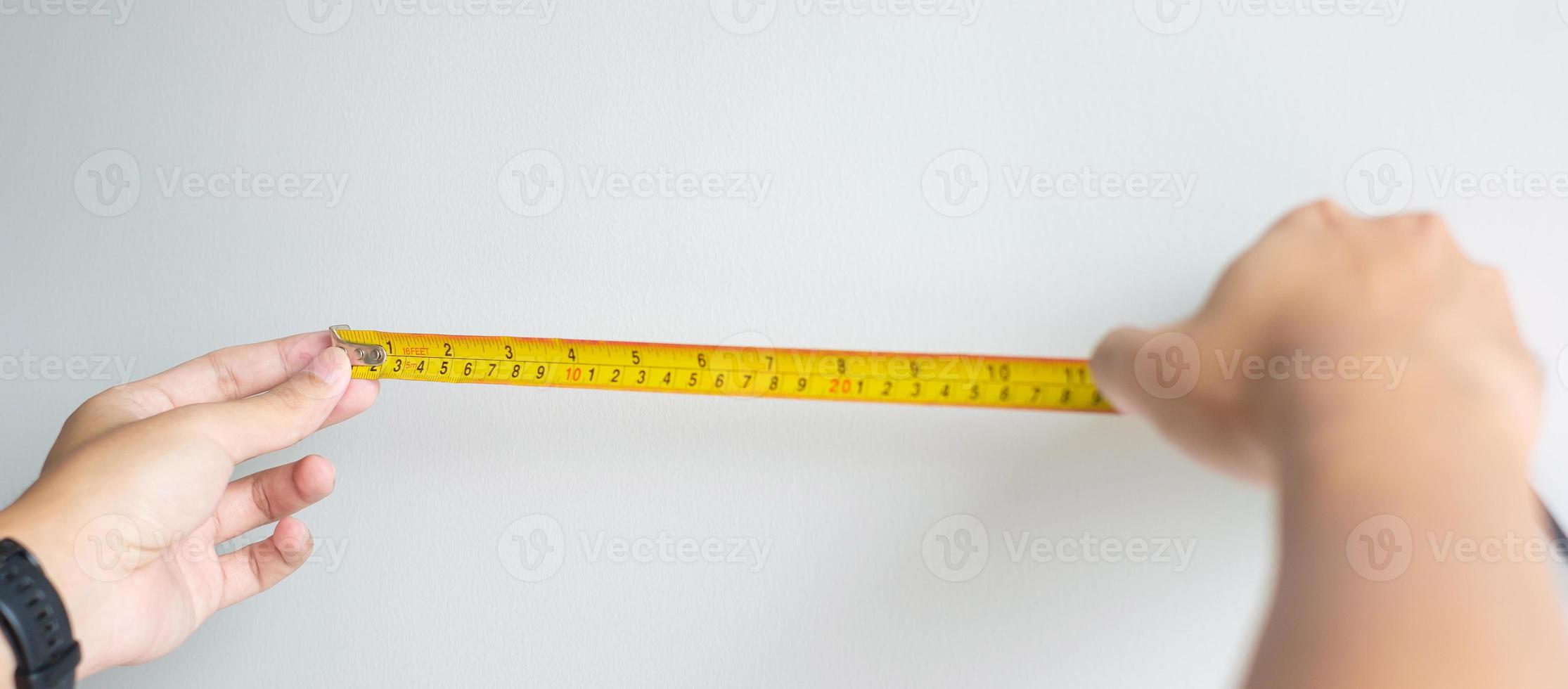 Man hand using tape measure for measuring with wall backgrounds at home. DIY, Interior design, repairing and improvement home or apartment concepts photo
