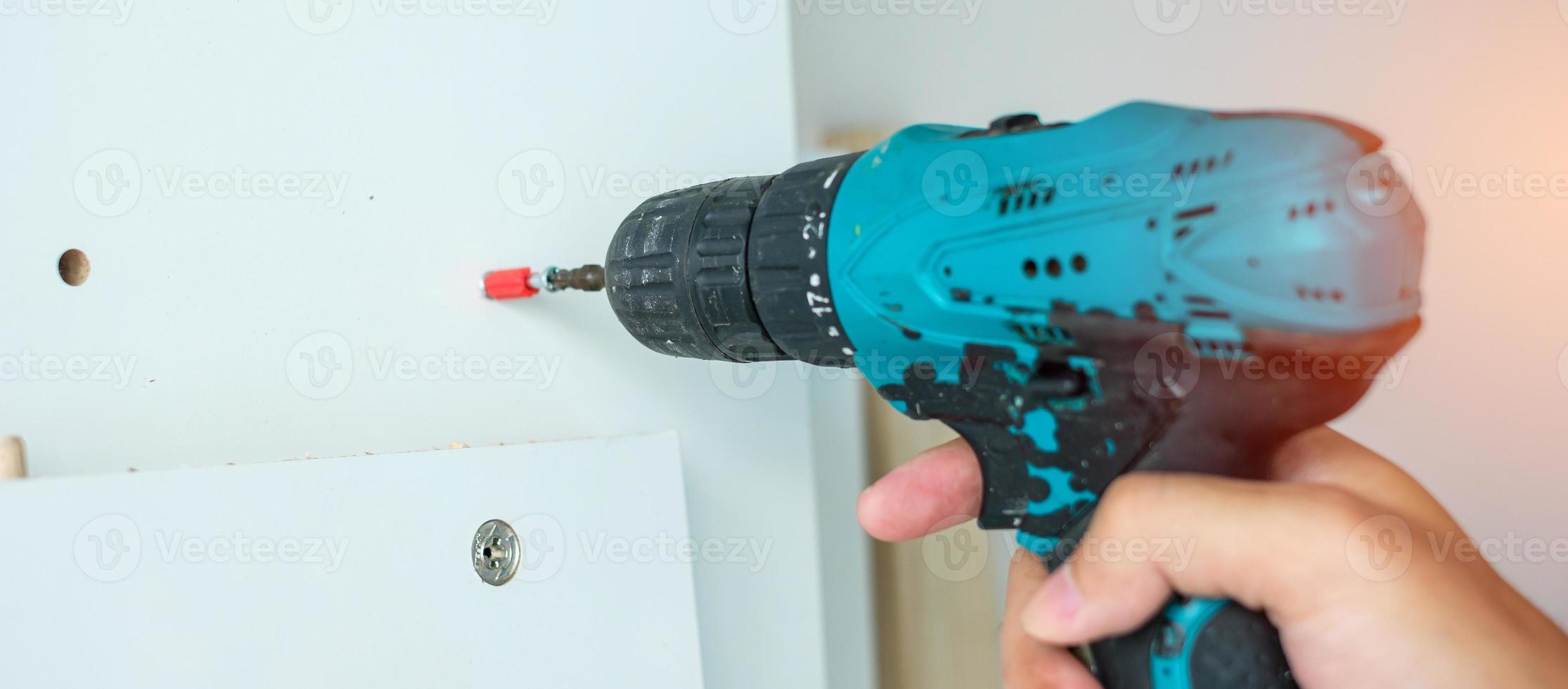 man using a cordless screwdriver assembling furniture at home, Carpenter working with electric screwdriver on the work photo