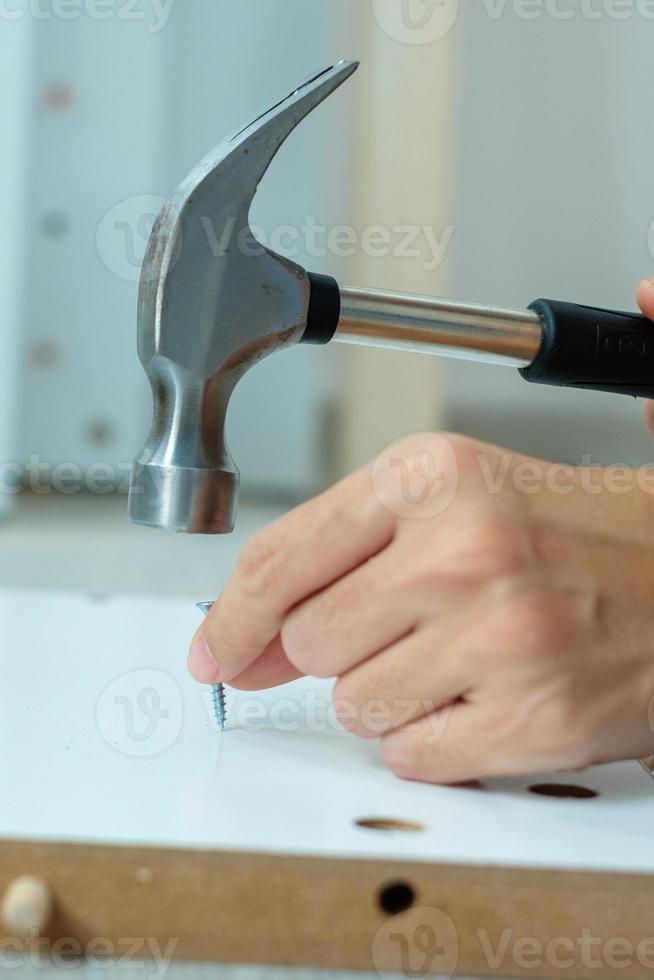 man using hammer hammering a nail into wooden boards, assembling or repairing furniture at home. DIY, Renovation, repairing and development home or apartment concepts photo