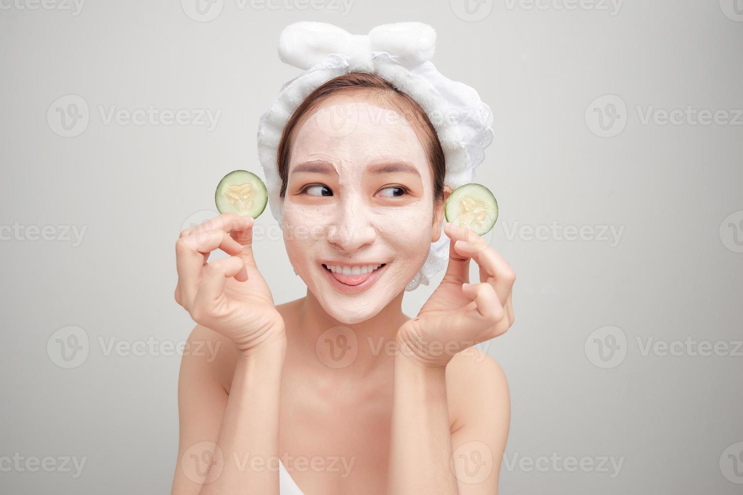 Beautiful girl holding a slice of cucumber in front of her face with mask of clay. photo