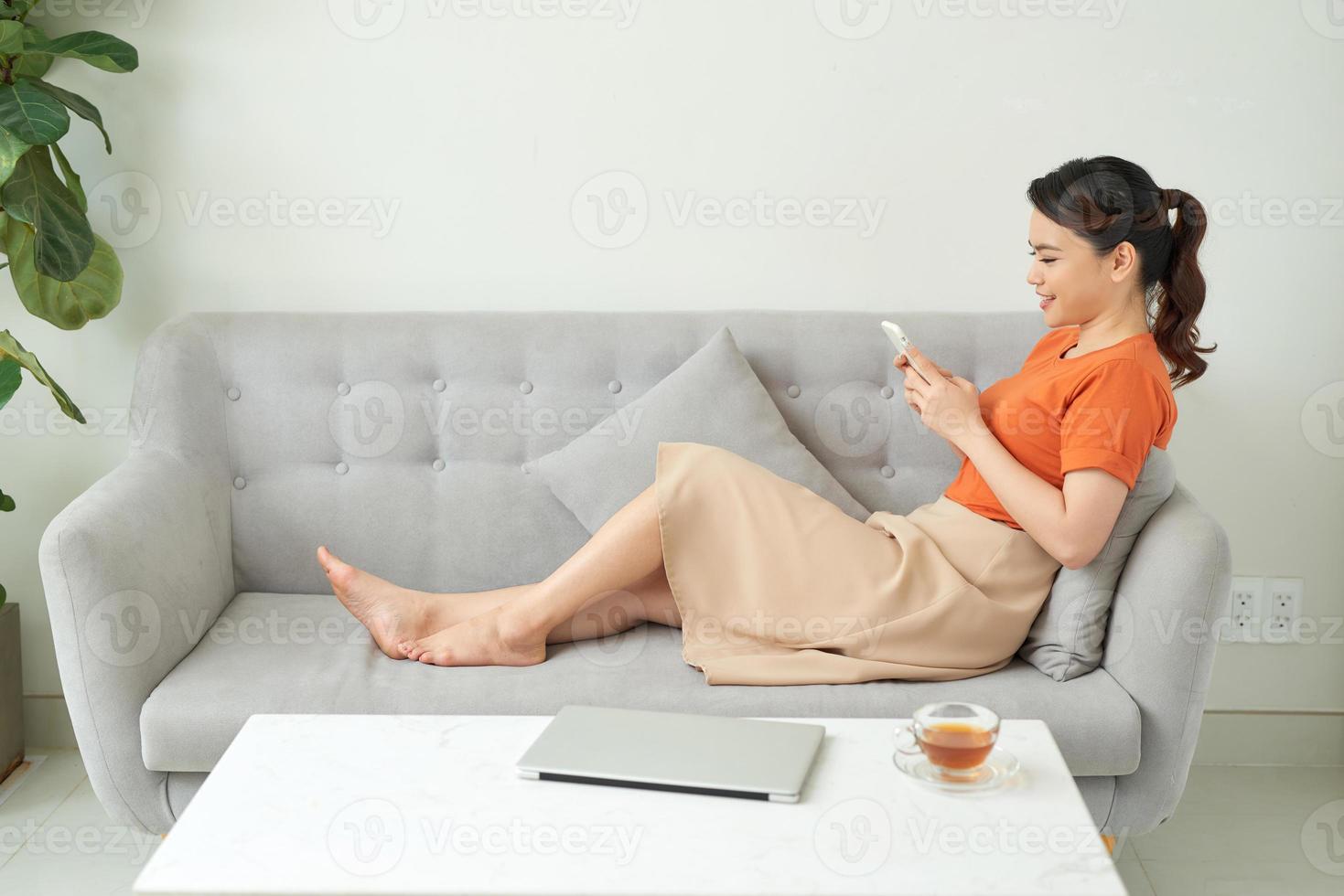 Casual young woman using laptop and cellphone on sofa at home photo