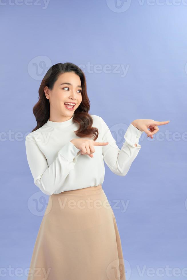 Young asian woman isolated on purple background shocked pointing with index fingers to a copy space. photo