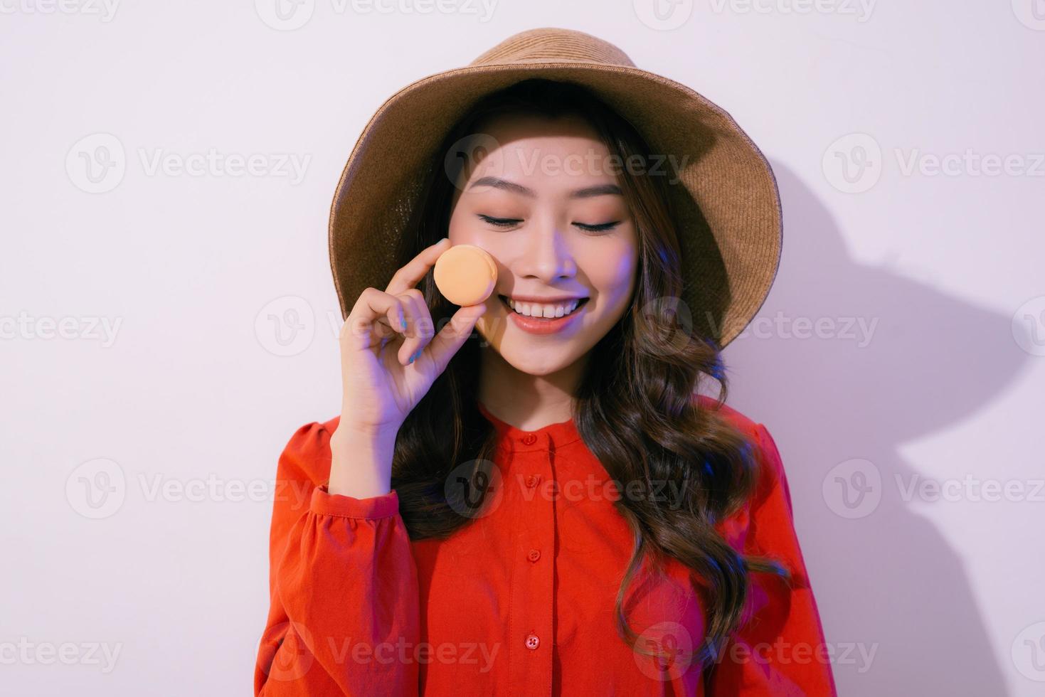 Portrait of a smiling woman with dark curly hair wearing red dress isolated over white background, showing macaroon photo