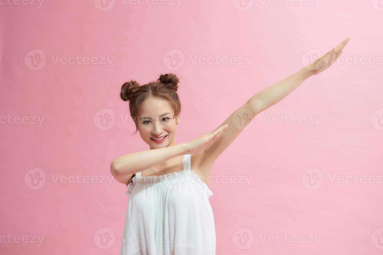 alegre y divertida mujer joven de 20 años haciendo un gesto de manos de baile de hip hop, en un retrato de estudio de fondo de color rosa pastel foto