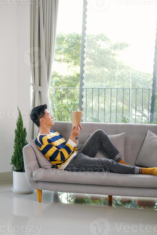 chico guapo leyendo un libro en el sofá con una amplia sonrisa foto