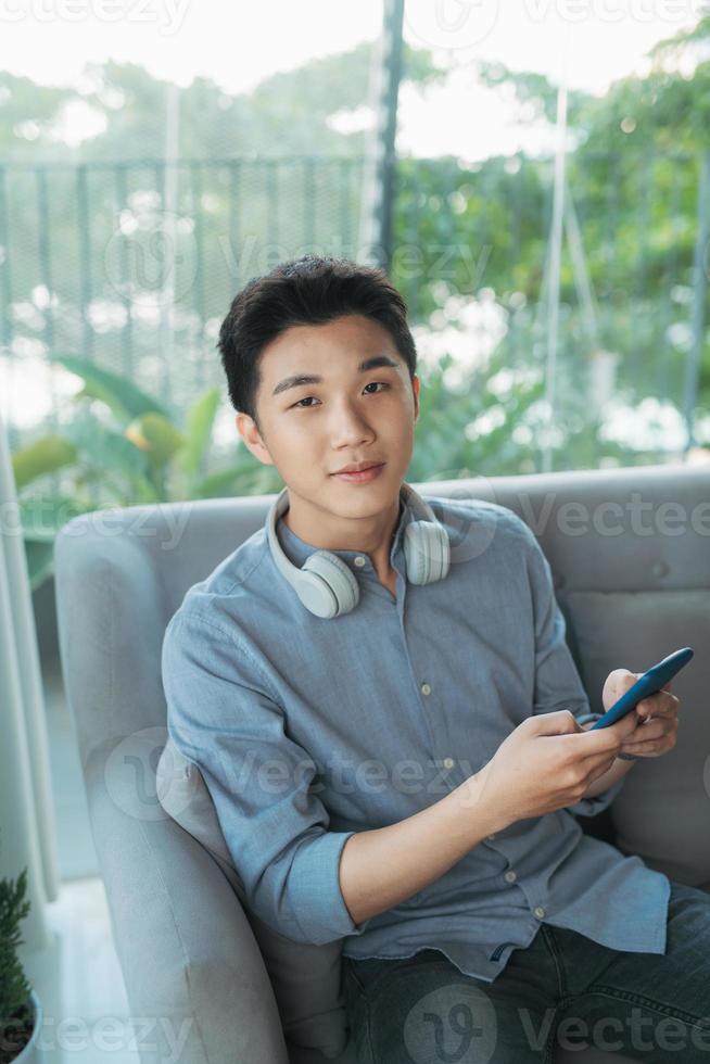 Young man leaning on sofa and playing games on phone at home photo