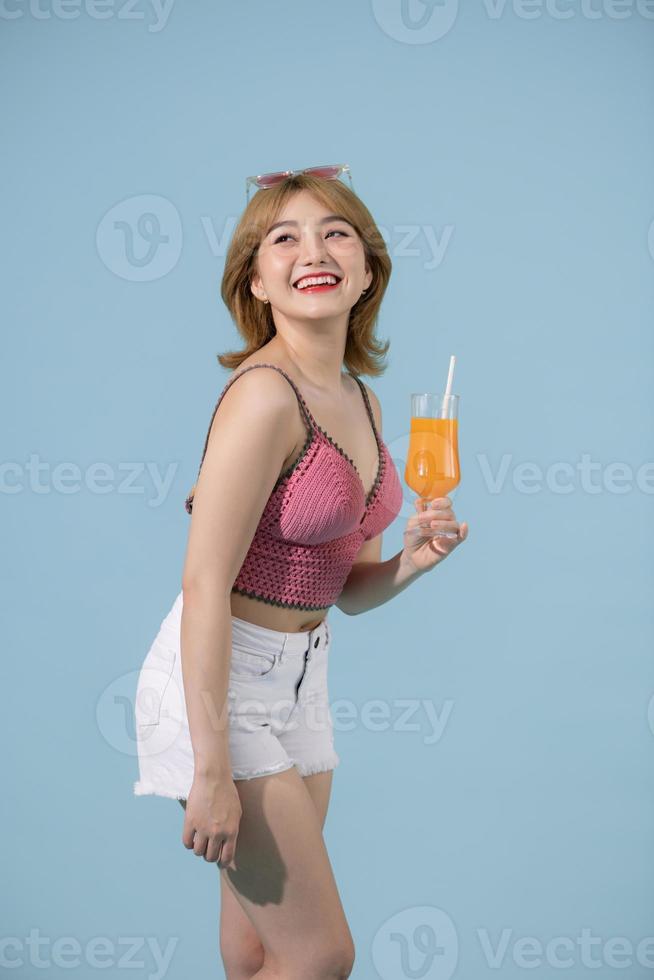 mujer asiática feliz con ropa informal de verano con un vaso de jugo de fruta fresca sobre fondo azul pastel foto