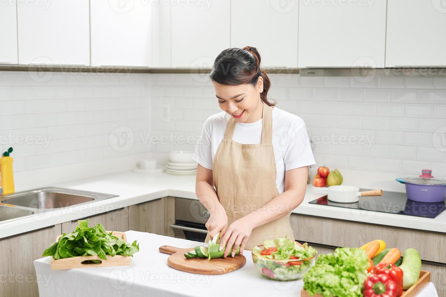 Young smiling housewife preparing healthy meal with vegetables in bright modern kitchen photo