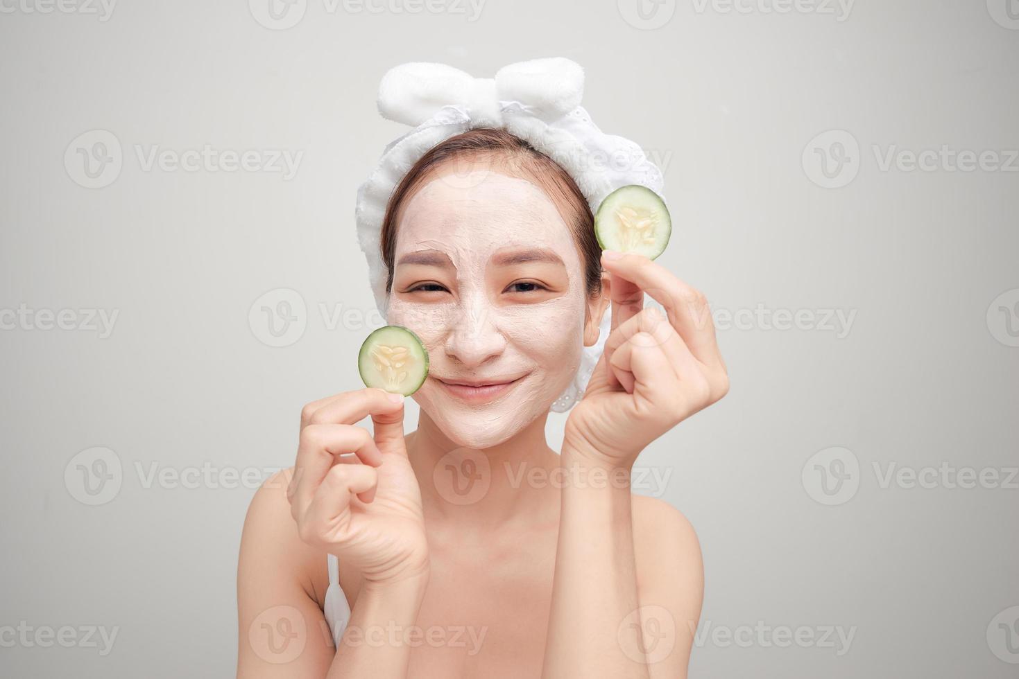 Beautiful young woman with facial mask on her face holding slices of fresh cucumber. photo