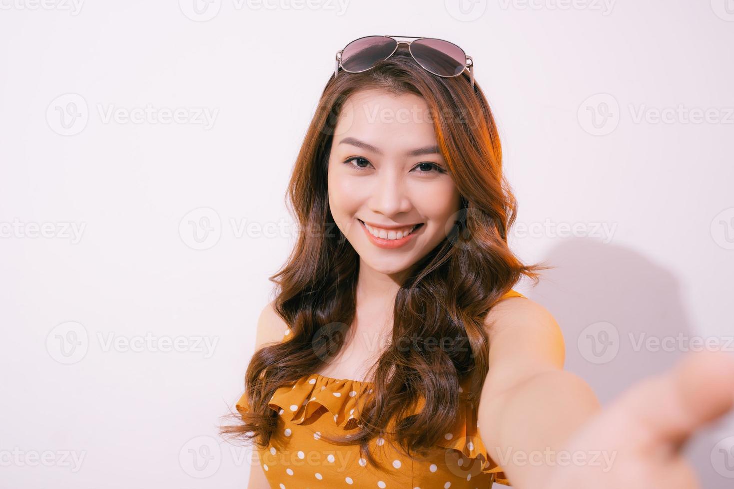 mujer joven de pie aislada en un fondo pastel tomando una foto selfie en un teléfono inteligente posando para la cámara sonriendo con dientes de cerca