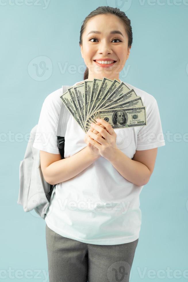 Happy girl student isolated on blue background, hold fan of cash money in dollar banknotes doing winner gesture photo