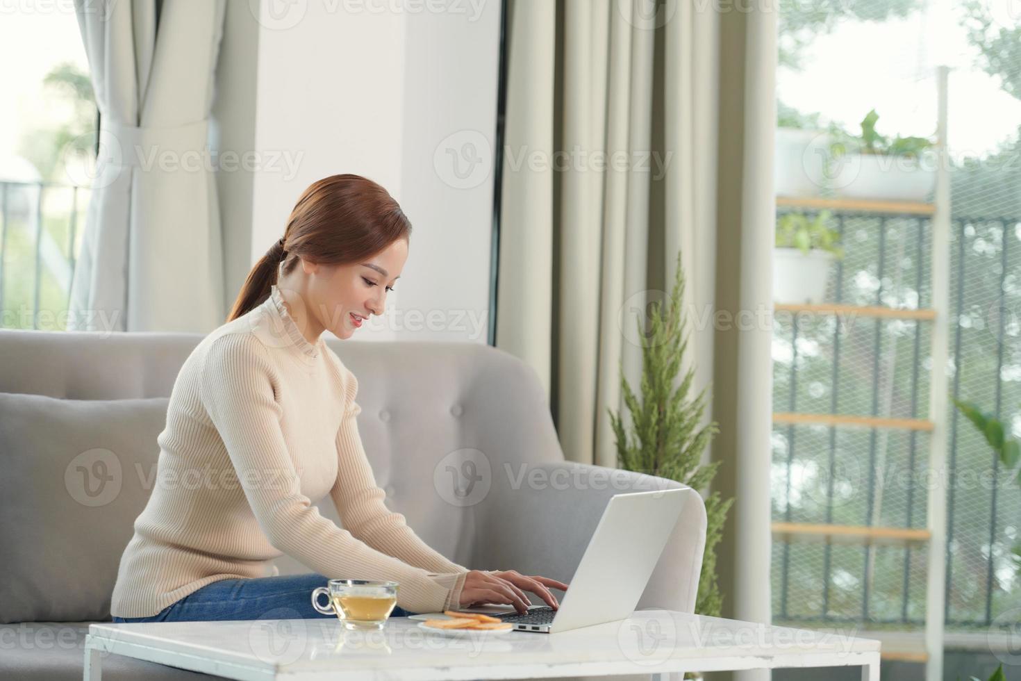 attractive smiling girl with cup of coffee using laptop at cozy home photo