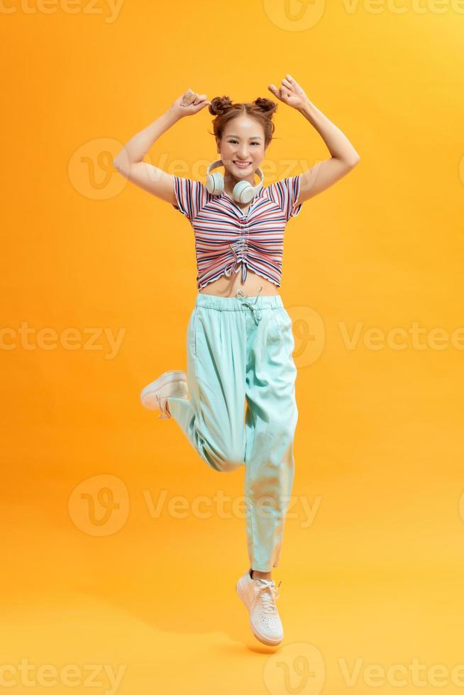 Young beautiful energy girl with white headphones listening to music laughs and jump on yellow background photo