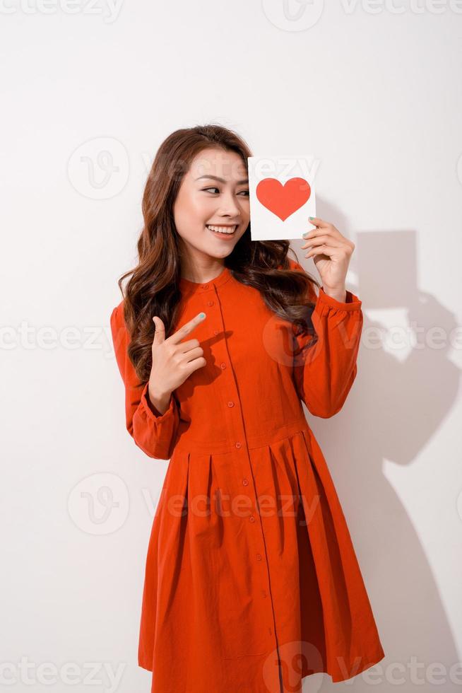 surprised asian young woman holding greeting card while standing isolated on pink photo