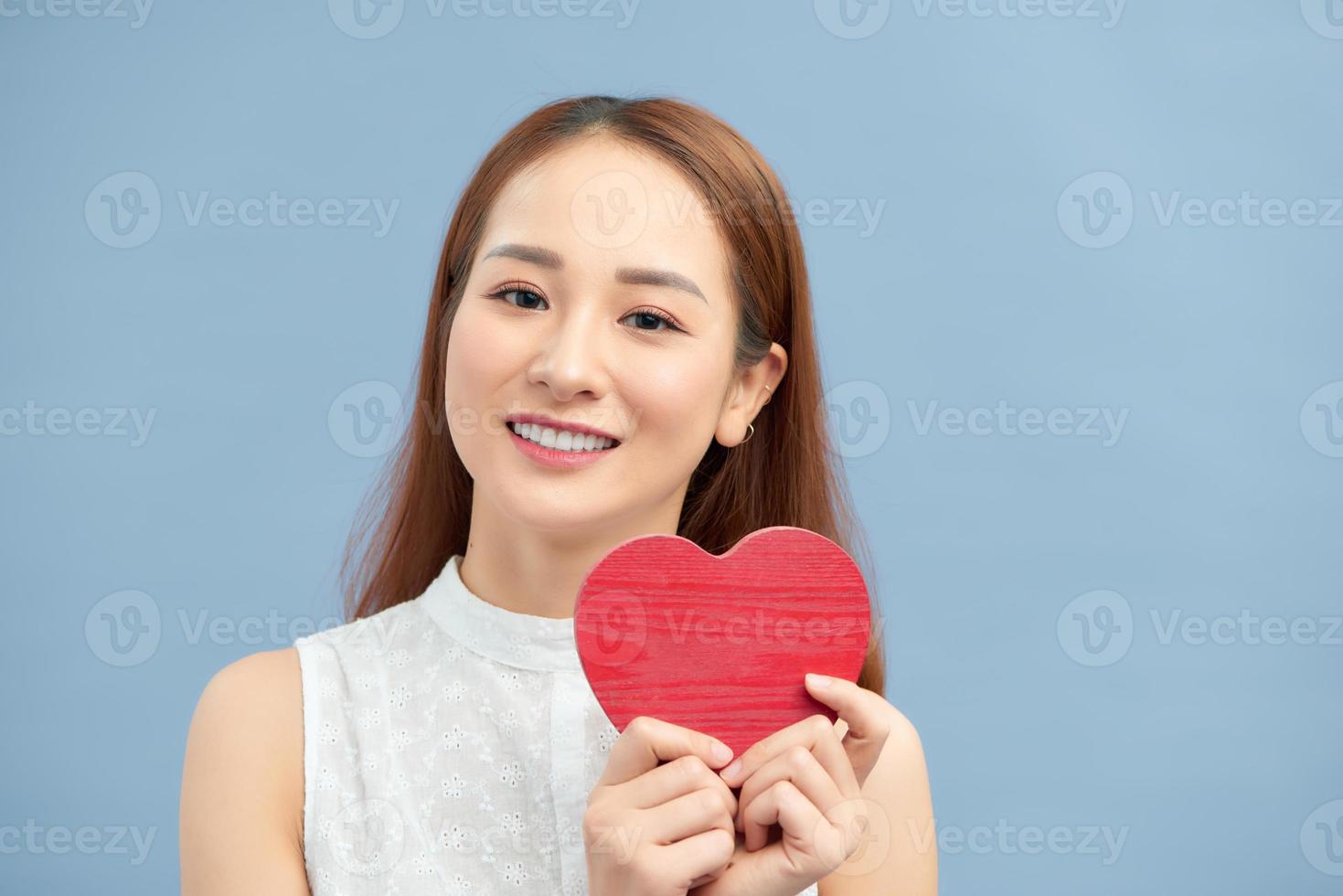 Happy woman hold red heart. Beautiful female model posing on isolated blue background. photo