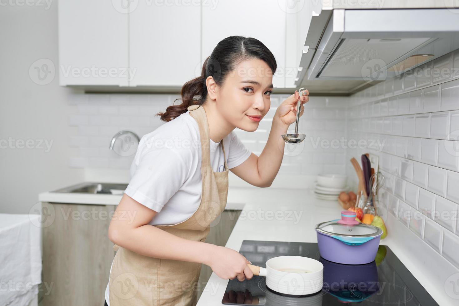 young woman is tasting her cooking in the kitchen photo