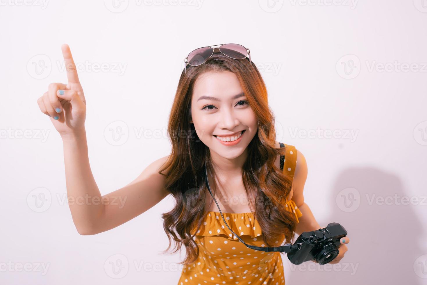 Close up portrait of a smiling pretty girl in dress taking photo on a retro camera isolated over pink background