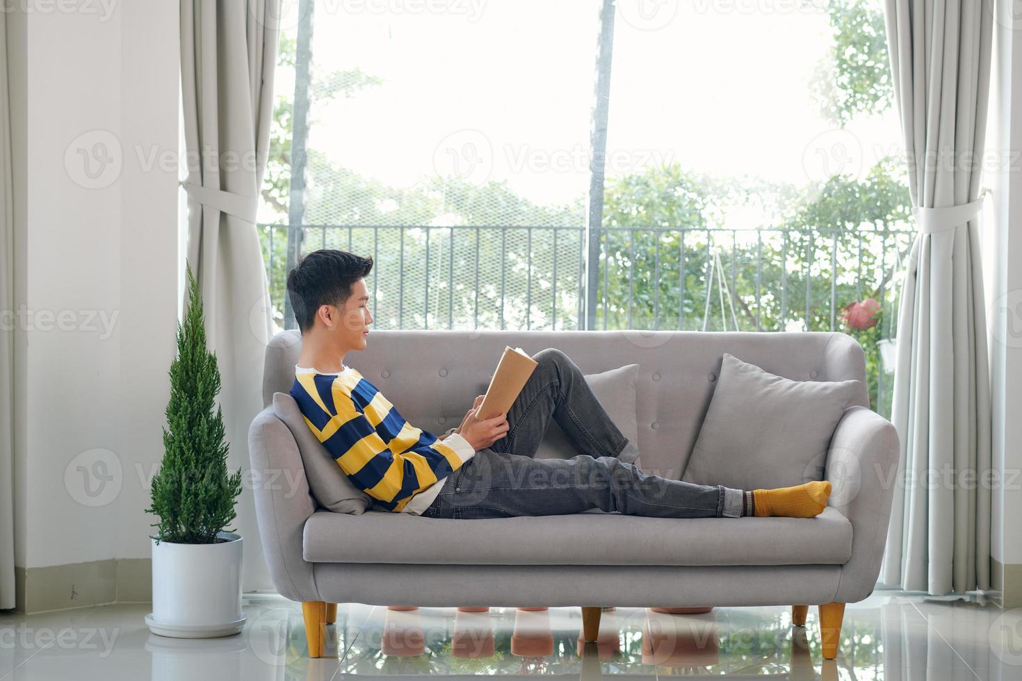 Young man reading book while sitting on the couch photo
