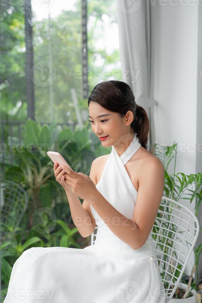 Happy Young Asian Lady Using Modern Smartphone While Resting At Home, photo