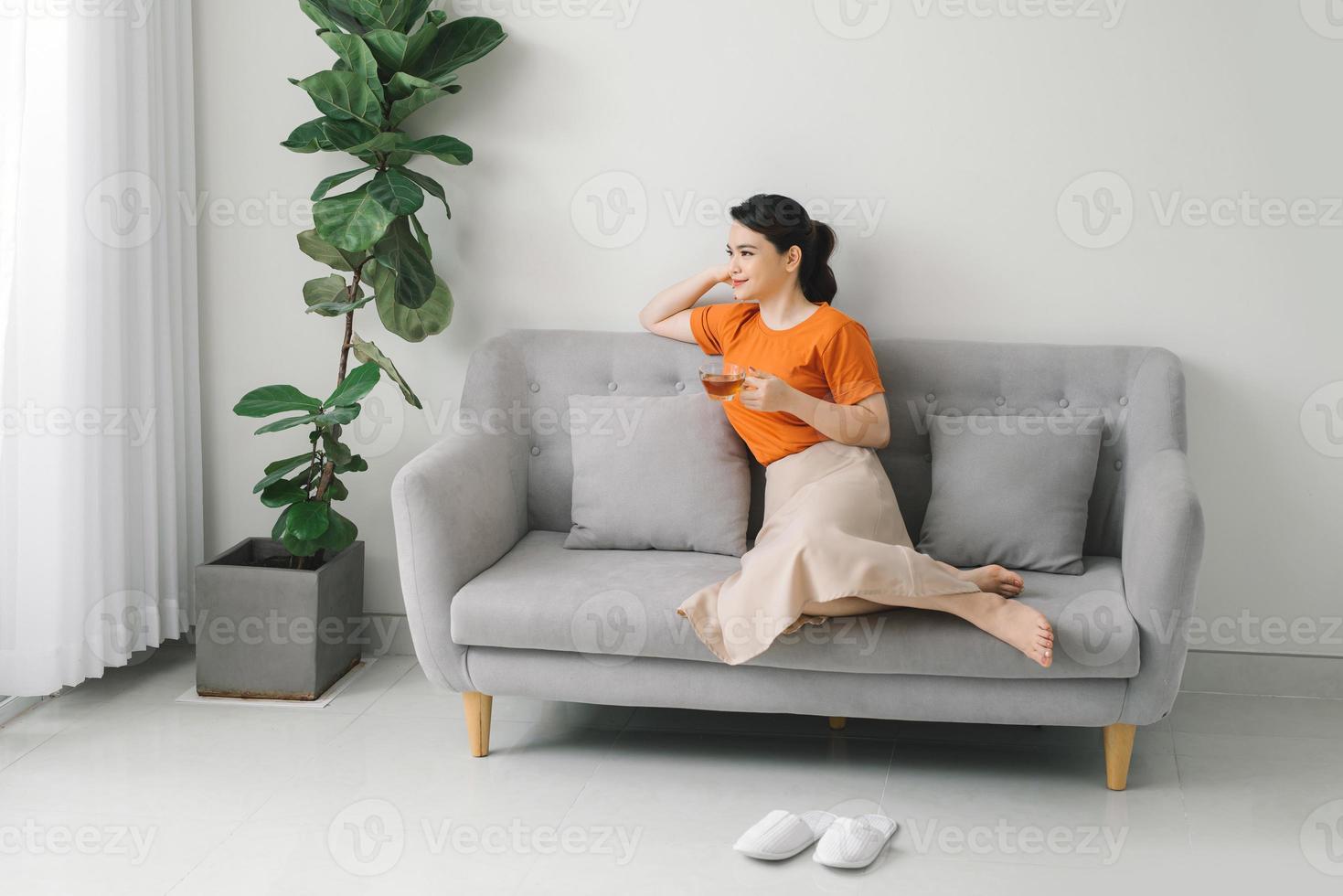 Attractive young woman drinking a cup of tea while relaxing on a sofa at home photo
