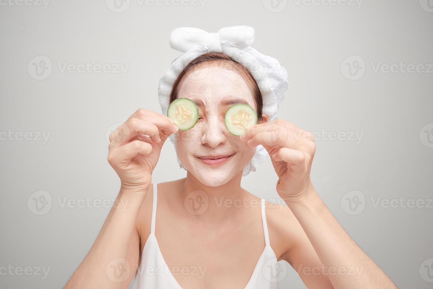 Young woman with clay facial mask holding cucumber slices isolated on white background photo